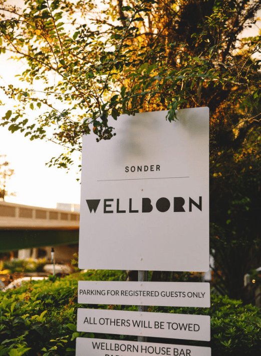the wellborn orlando white sign with black lettering in front of building and trees